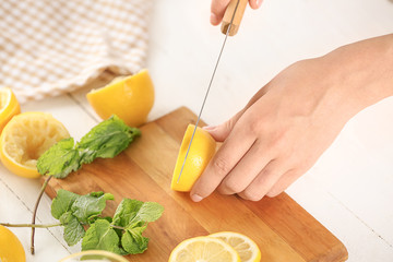 Woman cutting fresh lemon for juice on table
