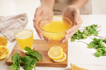 Woman holding glass bowl of fresh lemon juice over table