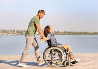 Happy young woman in wheelchair and her husband near river