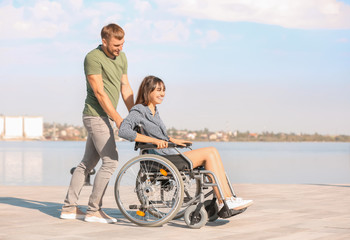 Naklejka premium happy young woman in wheelchair and her husband near river