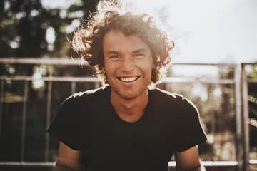Fotobehang Outdoor closeup portrait of handsome freckled smiling male with curly hair, posing for social advertisement, in the city street on sunset sunlight with copy space for your promotional information © iuricazac