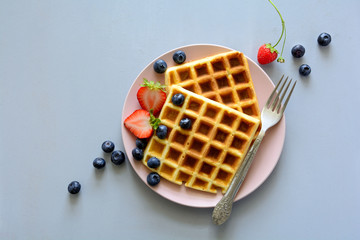 Belgian waffles with strawberries and blueberries on pink plate on gray wooden background. Top view. Copy space - Powered by Adobe