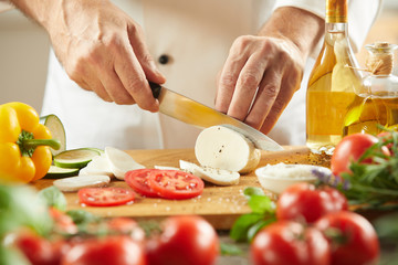 Chef cutting fresh cheese with tomatoes
