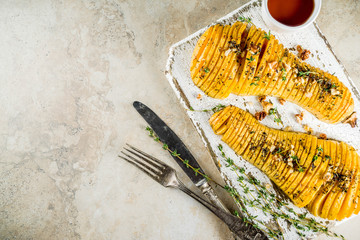 Simple autumn domestic recipes, roasted hasselback butternut squash pumpkin with thyme, honey and maple syrup, on light background copy space top view