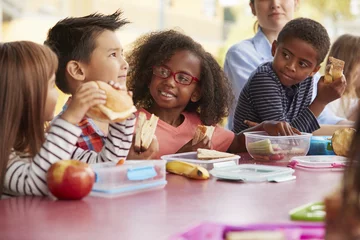 Fotobehang Young school kids eating lunch talking at a table together  © Monkey Business