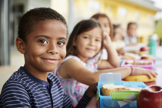 Young boy and girl at school lunch table smiling to camera