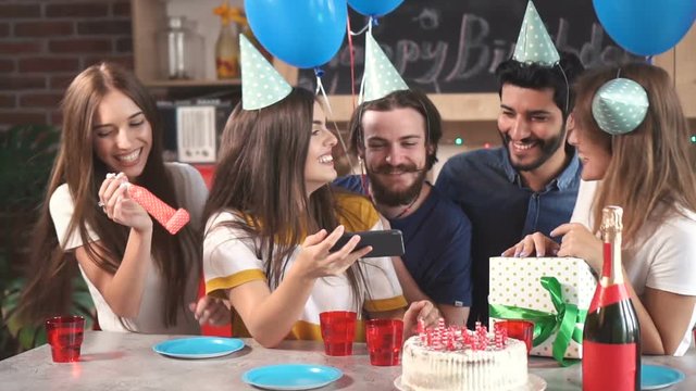 Joyful lovely friends looking at taken photos on smartphone, having great fun at birthday party, slowmotion in well-furnished cozy kitchen