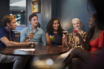 Group Of Young Friends Sitting Around Table In Bar Together On Night Out