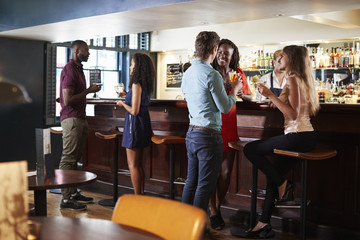 Group Of Young Friends Relaxing In Bar Standing At Counter
