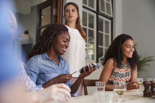 Female Customer In Restaurant Paying Bill Using Contactless Credit Card Terminal