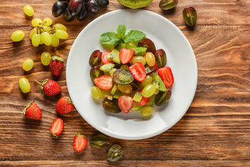 Plate with delicious fruit salad on wooden table