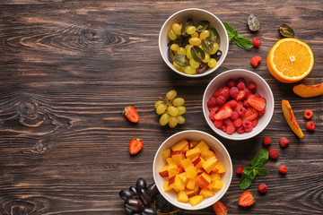 Bowls with fresh fruits and berries on wooden table