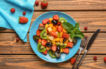 Plate with delicious fruit salad and mint on wooden table