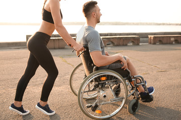Sporty woman helping young man in wheelchair outdoors