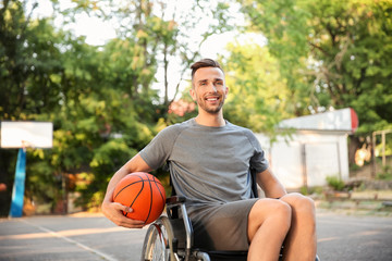 Sporty young man with ball sitting in wheelchair outdoors
