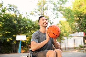 Fototapeta premium Sporty young man with ball sitting in wheelchair outdoors