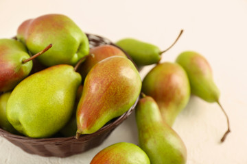 Wicker bowl with ripe sweet pears on white table
