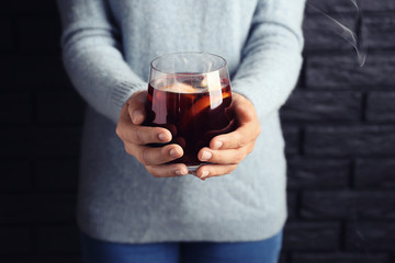 Woman holding glass of delicious hot mulled wine on brick wall background