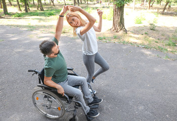 Man in wheelchair with beautiful woman dancing outdoors