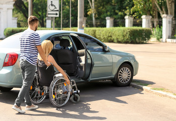 Naklejka premium Man helping woman in wheelchair to sit in car