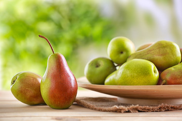 Plate with ripe pears on table against blurred background