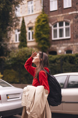 Portrait of woman wearing red hoodie and black bag back while holding beige trench coat in her arm and enjoy landscape. tourist girl walk in the city.