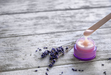 Stick with body cream over jar on wooden table