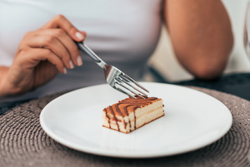 Close-up image close up of woman eating cake with a fork and sitting at table.