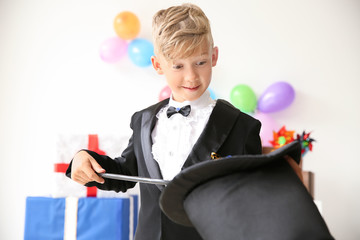 Cute little magician showing tricks with hat indoors