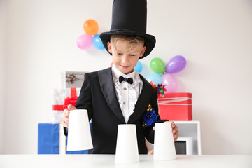 Cute little magician showing tricks with cups indoors - obrazy, fototapety, plakaty