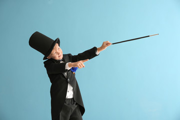 Cute little magician showing trick on color background
