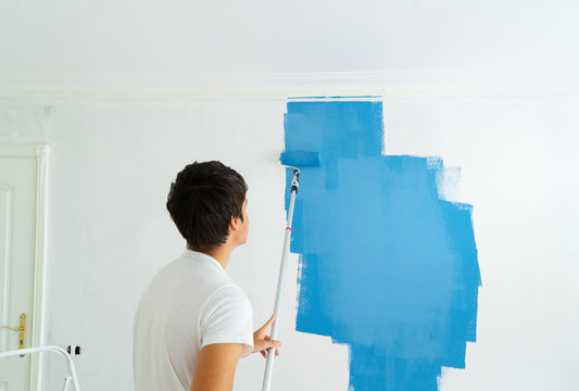 young man painting wall in blue color in the white plastered room