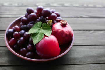 Plate with sweet grapes and pomegranates on wooden table
