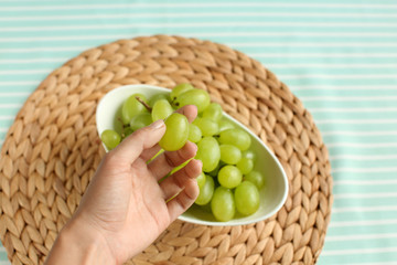Woman taking sweet grapes from bowl on table