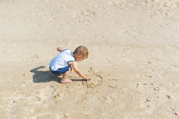 Fototapeta na wymiar Baby boy draws a sun in the sand on the beach.