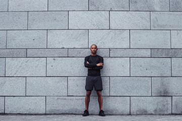 Handsome sportsperson. Full length of young man in sportswear standing against grey background outdoors