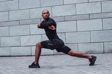 Stretching key to wellbeing. Full length of young man in sportswear doing stretching against grey background outdoors