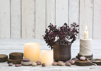 Rustic decoraton with candles, old reel and elderberries in a vase on a white wooden background, perfect for scandi-chic style winter and autumn mood