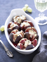 Figs baked with goat cheese, walnuts, honey and thyme on dark blue background.