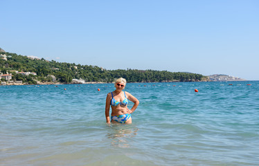 Aged woman is standing in water of Sutomore beach, Montenegro.