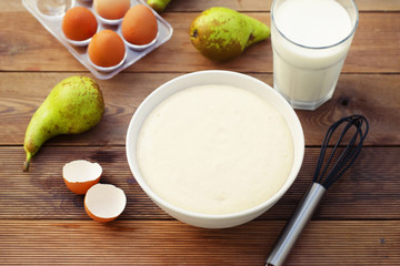 Ingredients for baking pie with pears. The process of making sweet pastries. Bowl with dough, glass of milk, eggs and pear fruits. Wooden table.