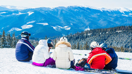 several skiers rest on the top of the mountain. A group of people in ski suits sitting on the snow s makes a selfie