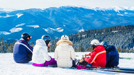 several skiers rest on the top of the mountain. A group of people in ski suits sitting on the snow s makes a selfie