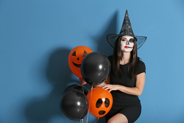 Beautiful woman dressed as witch for Halloween with balloons on color background