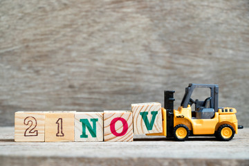 Toy forklift hold block V to complete word 21nov on wood background (Concept for calendar date 21...
