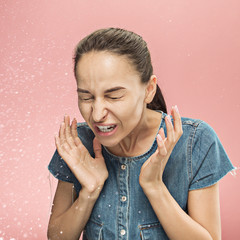 Young funny woman sneezing with spray and small drops, studio portrait on pink background. Comic,...
