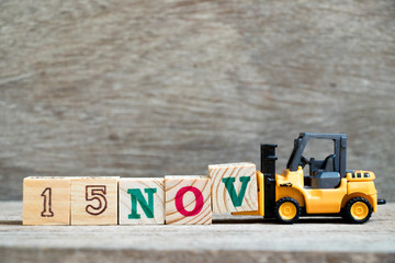Toy forklift hold block V to complete word 15nov on wood background (Concept for calendar date 15 in month November)