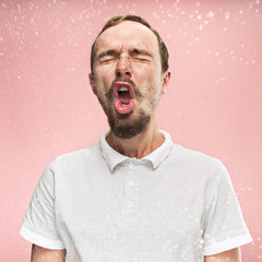 Young funny handsome man with beard and mustache sneezing with spray and small drops, studio...