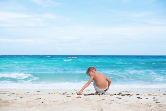boy playing with natural sticks. blue sea white sand