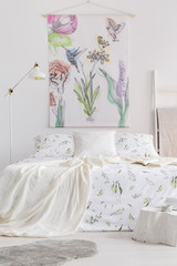 Vertical view of a scandinavian style bedroom interior with a bed dressed in white linen with painted green plants. Fabric wall art with colorful birds and flowers above the bed. Real photo.